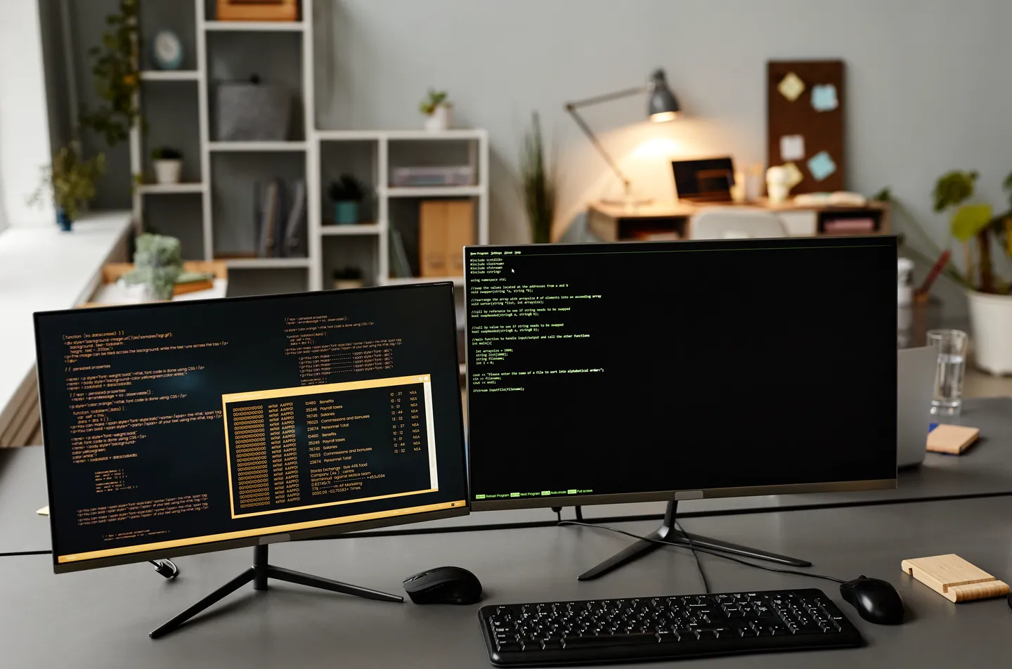 Two monitors showing code on a desk, with a keyboard and mouse, in a bright home office.